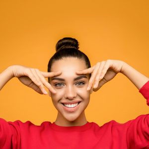 Happy woman in red sweatshirt poses playfully against an orange backdrop, showcasing fashion and joy.