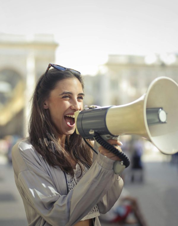 Cheerful young woman in a casual outfit shouting into a megaphone on a sunny day.
